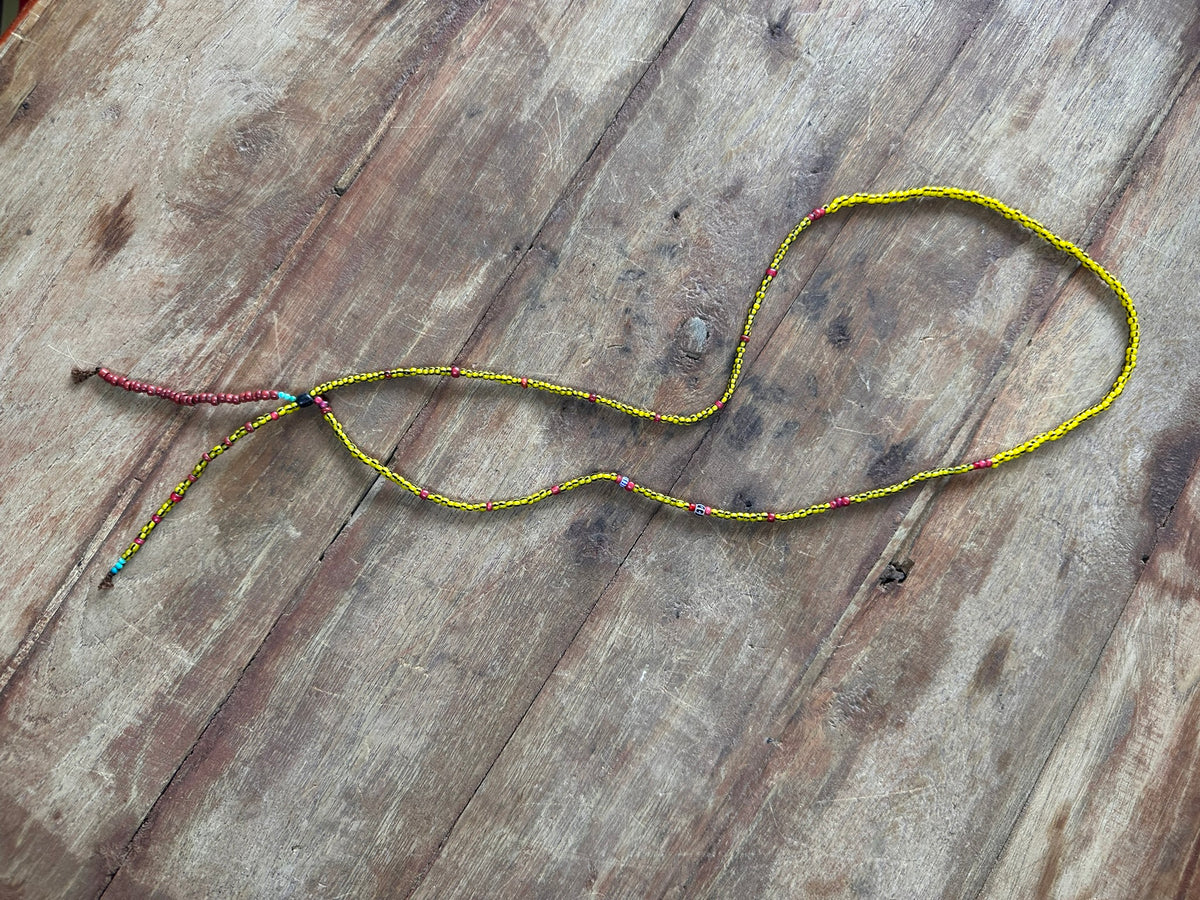 A beaded necklace with a yellow and black patterned strand, accented with small red and blue beads, laid out on a rustic wooden surface.