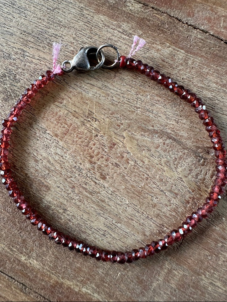 A beaded bracelet made of faceted dark red beads with a silver-toned lobster clasp, photographed on a rustic wooden surface.