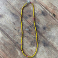 A beaded necklace made of small yellow beads with a few pink accent beads and a silver clasp, laid flat on a rustic wooden surface.