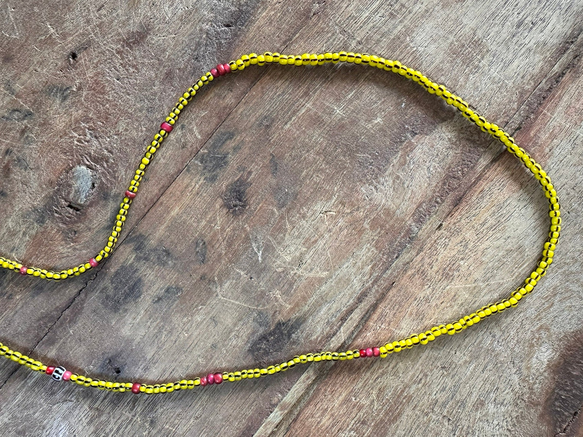 A yellow braided cord necklace with small red and purple beads, laid out on a rustic wooden surface.