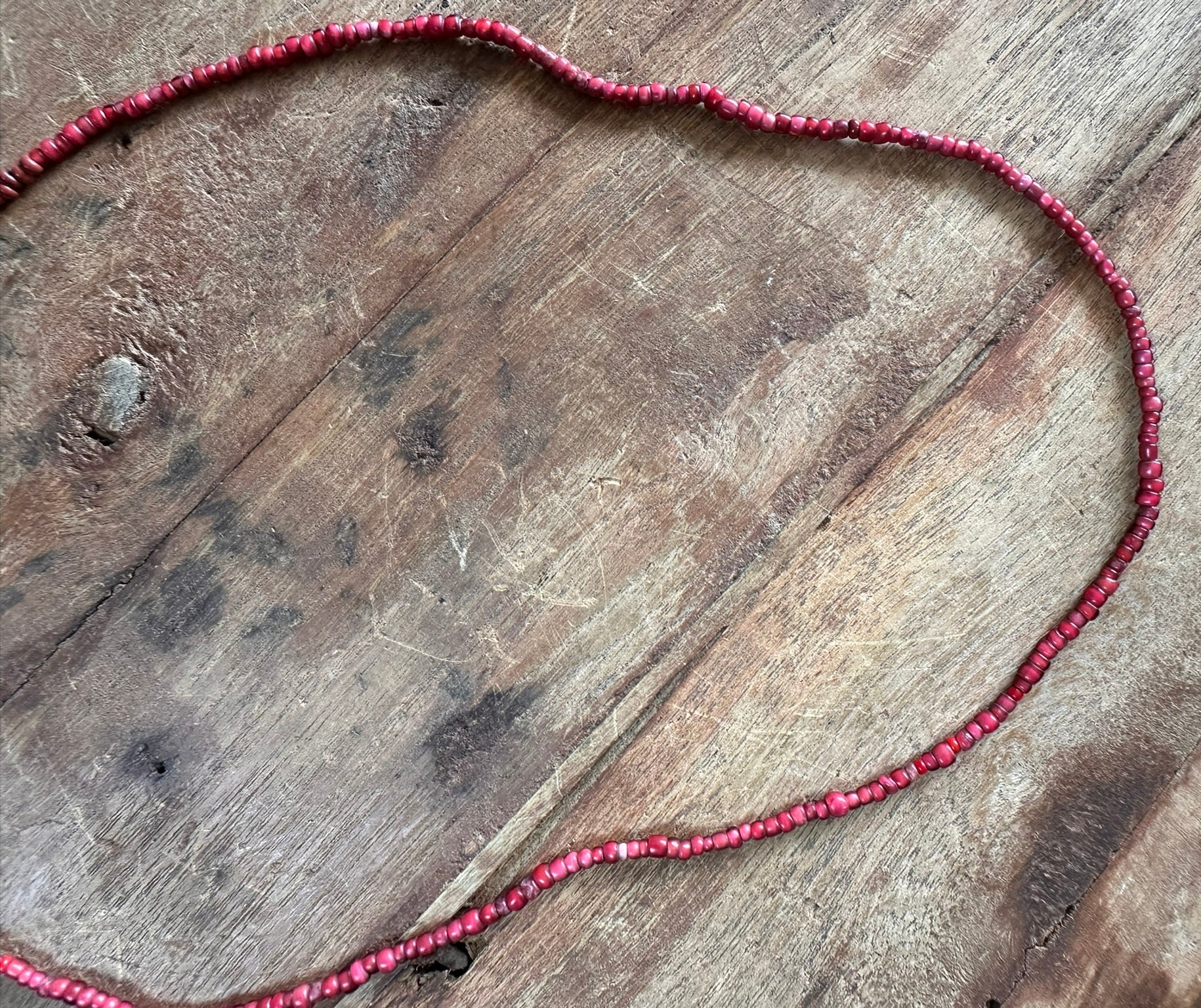A strand of small red beads arranged in an irregular loop on a rustic brown wooden surface.