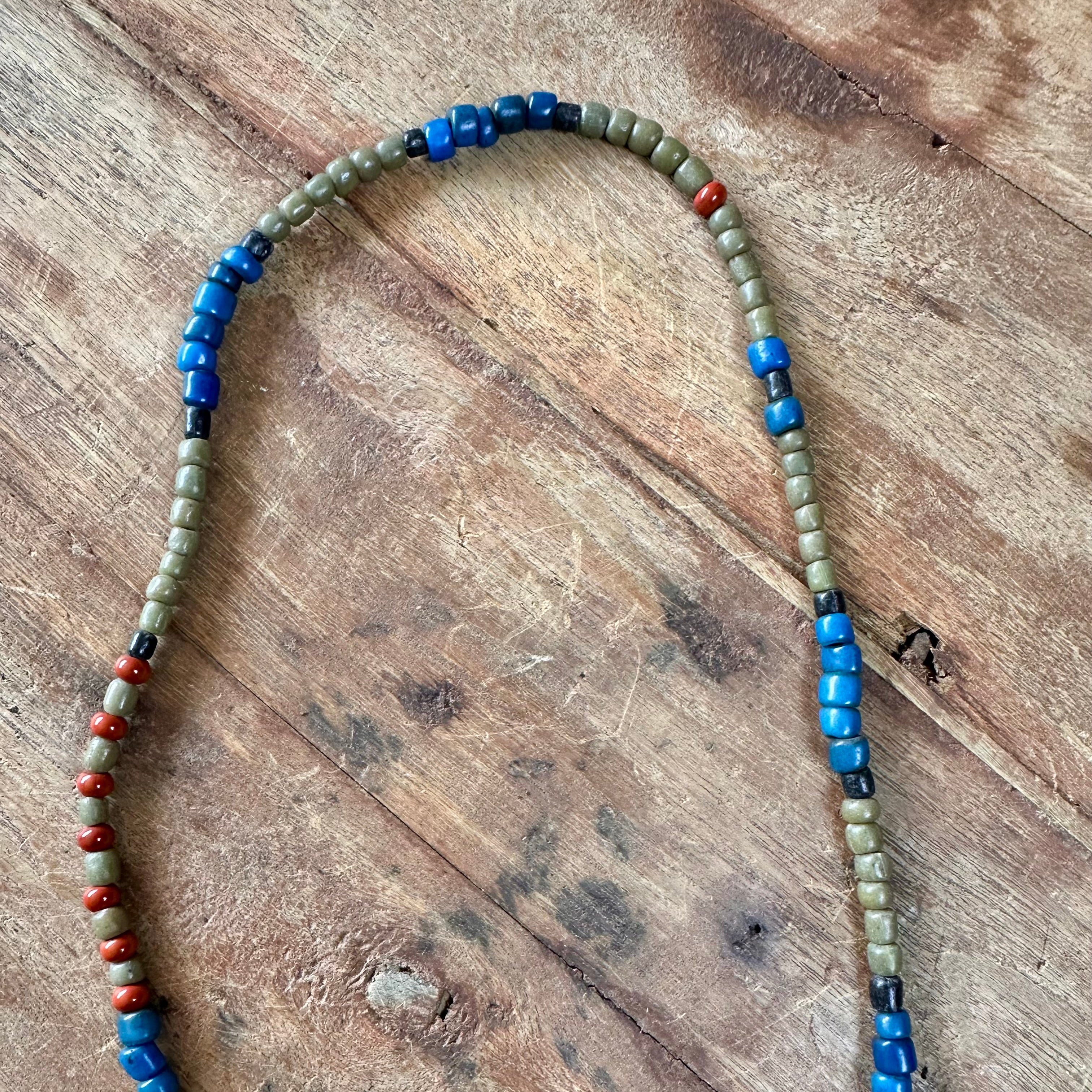 A beaded necklace with alternating sections of blue beads, small red beads, and olive-green beads, laid out on a rustic wooden surface.