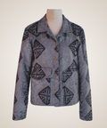 A long-sleeve button-front jacket displayed on a mannequin torso against a plain light beige background. The jacket has a muted gray-purple base with a dark geometric tribal-style pattern and small brown buttons.