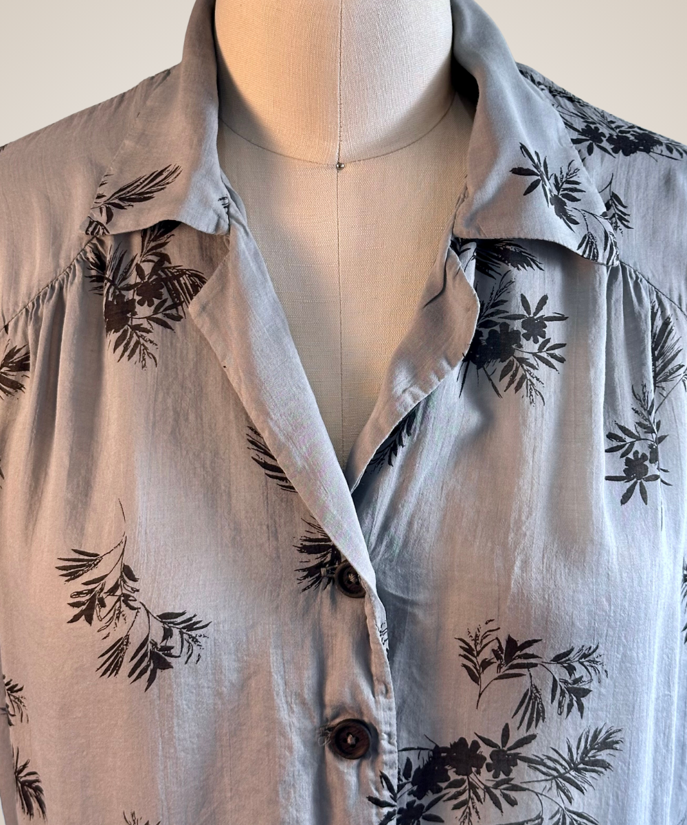 A close-up of a light gray button-up shirt with a black floral and leaf print, displayed on a cream-colored dress form mannequin.