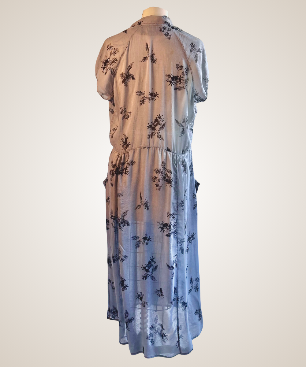 A sheer midi dress with a short-sleeve collar, shown from the back on a mannequin. The dress features a gradient color story, starting with a light taupe-beige at the top and fading into a soft sky blue at the bottom, decorated with a dark navy floral pattern.