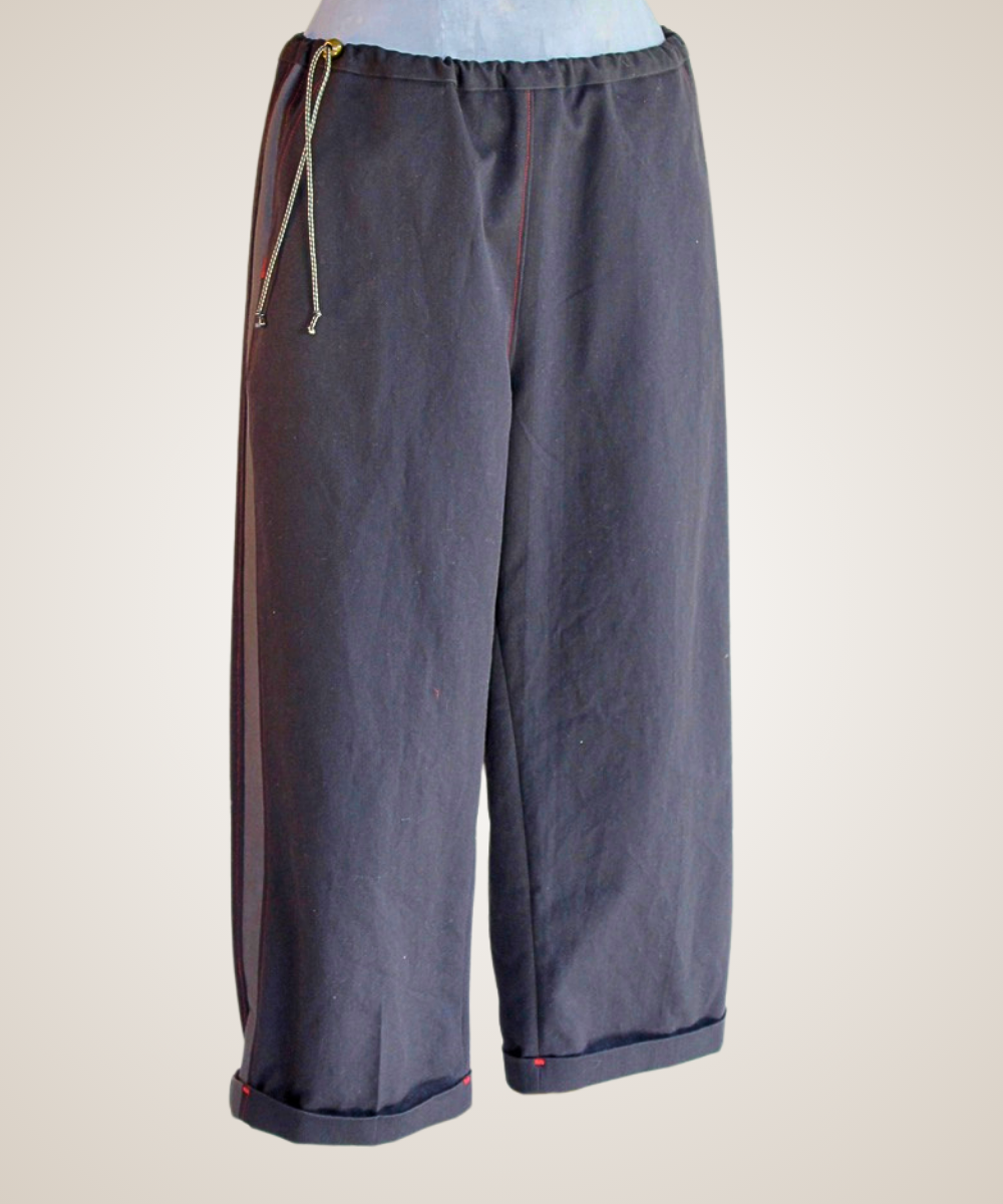A pair of wide-leg cropped pants in a dark slate gray fabric, featuring a drawstring waist and a thin red piping detail along the side seams, shown against a plain light beige background.