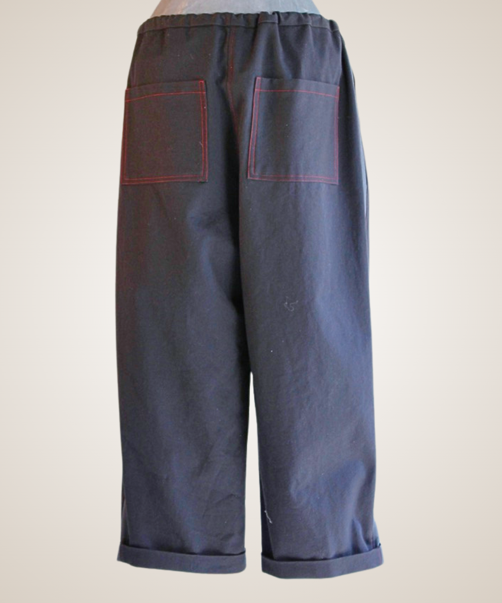 A pair of dark blue cropped pants shown from the back, featuring two large patch pockets with red contrast stitching and rolled cuffs.