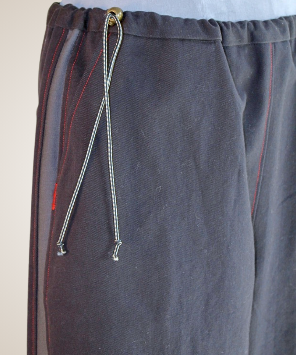 Close-up of dark gray drawstring pants with red contrast stitching and a white-and-gray drawstring cord, shown against a plain light background.
