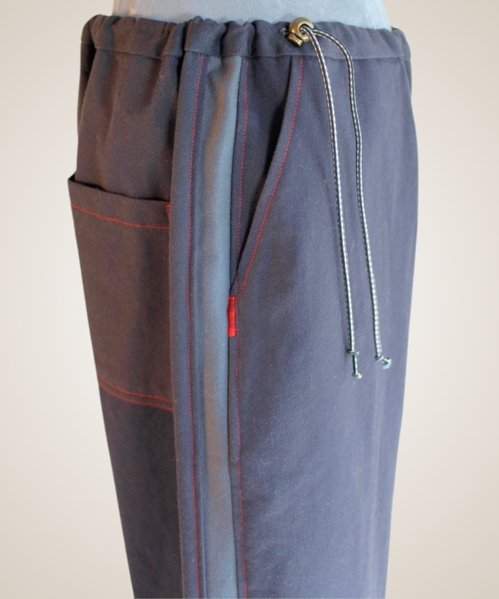 A close-up of a pair of wide-leg pants displayed on a mannequin torso. The pants feature a split design: one side has a brown leather patch pocket and a brown-and-beige abstract print, while the other side is a solid dark brown suede-like fabric.
