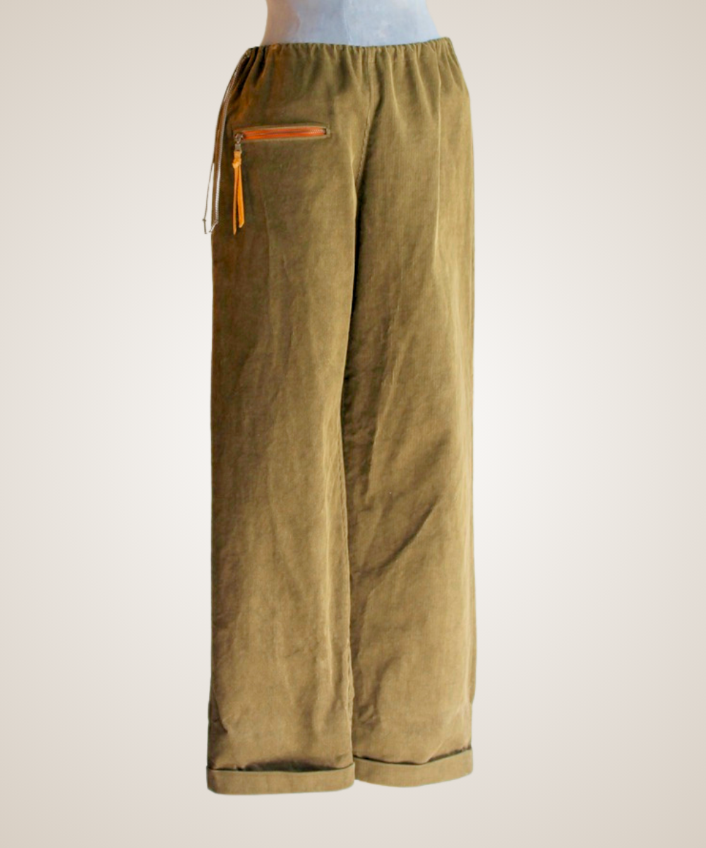 A pair of wide-leg trousers in olive green corduroy fabric, featuring an elastic drawstring waist and a zippered pocket on the left side, displayed on a mannequin against a light beige background.