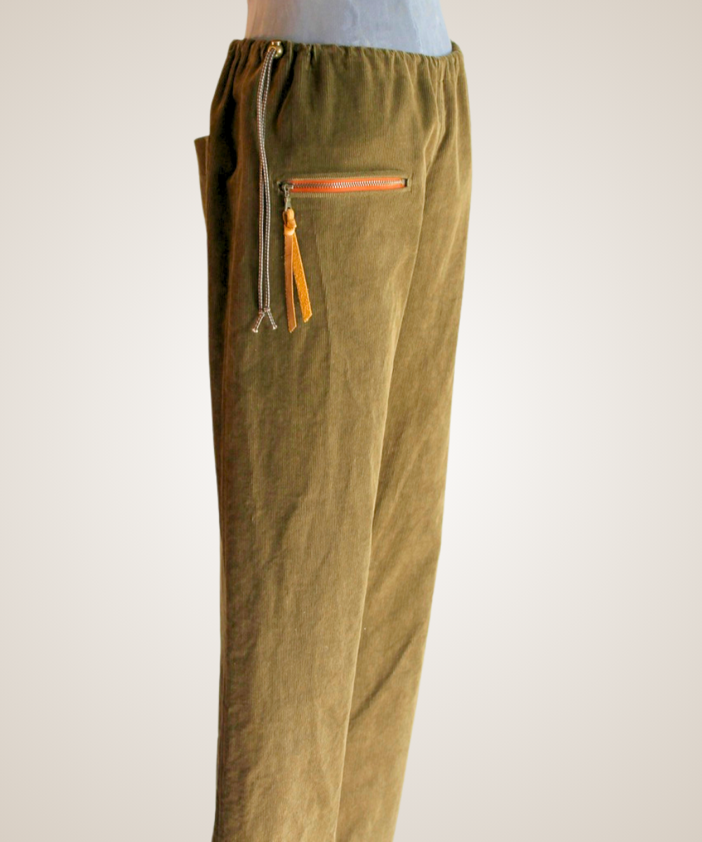 Olive green corduroy pants with a drawstring waist, side pocket, and orange zipper accent, shown on a mannequin against a light background.