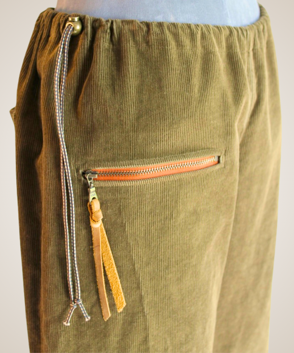 Close-up of olive green corduroy pants with a drawstring waist and a zippered pocket featuring a tan leather tassel.
