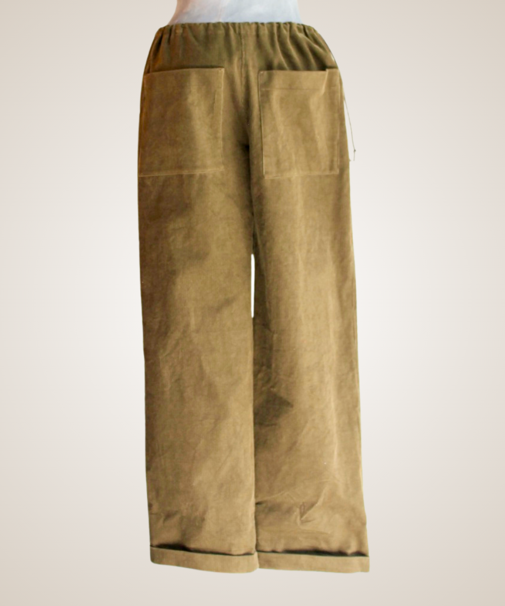 A close-up of a pair of wide-leg pants displayed on a mannequin torso. The pants feature a split design: one side has a brown leather patch pocket and a brown-and-beige abstract print, while the other side is a solid dark brown suede-like fabric.
