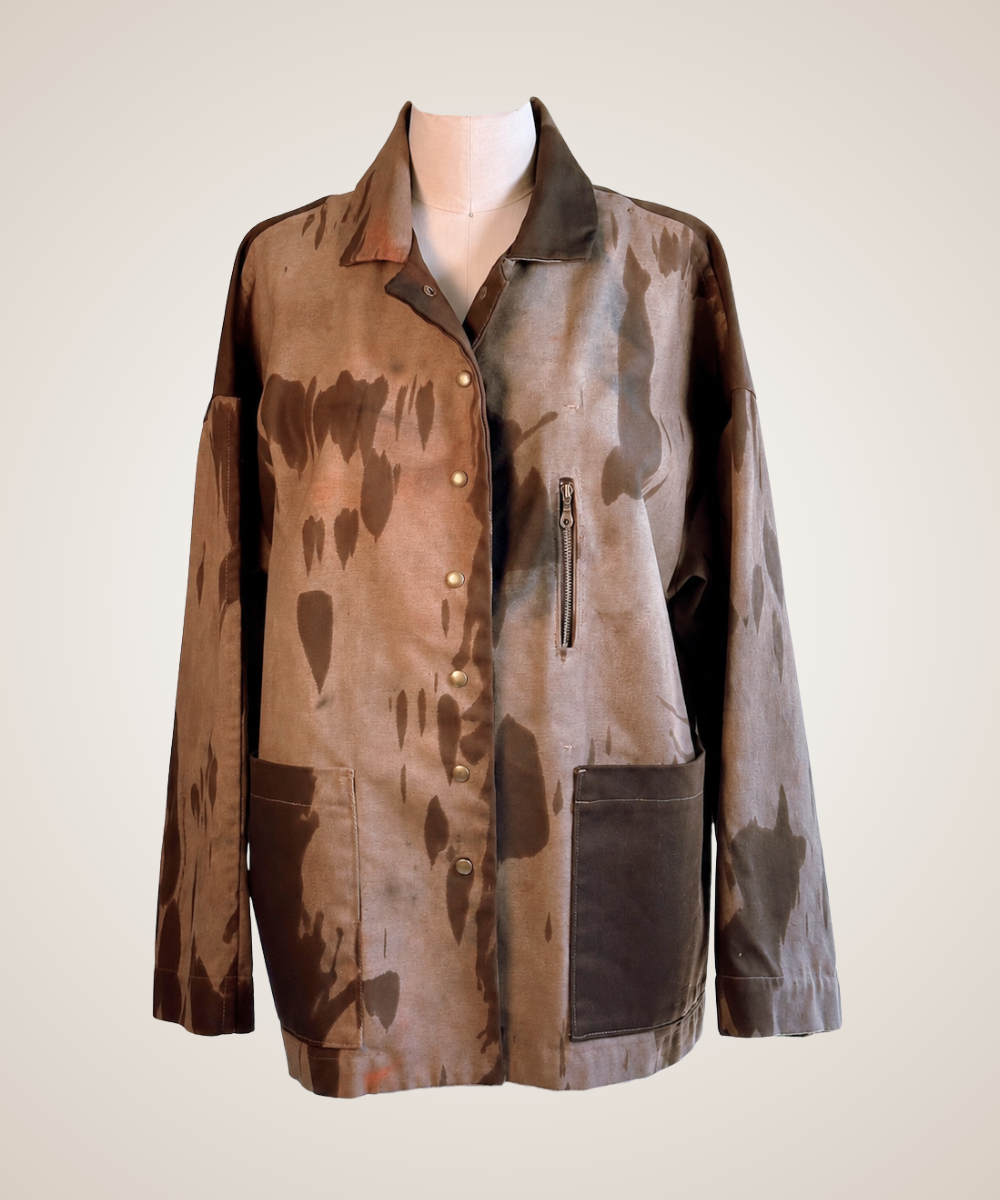 A long-sleeve button-front jacket displayed on a mannequin torso against a plain light beige background. The jacket has a mottled brown and taupe pattern with solid dark brown pocket panels and a dark brown collar, plus a vertical zip pocket on the chest.