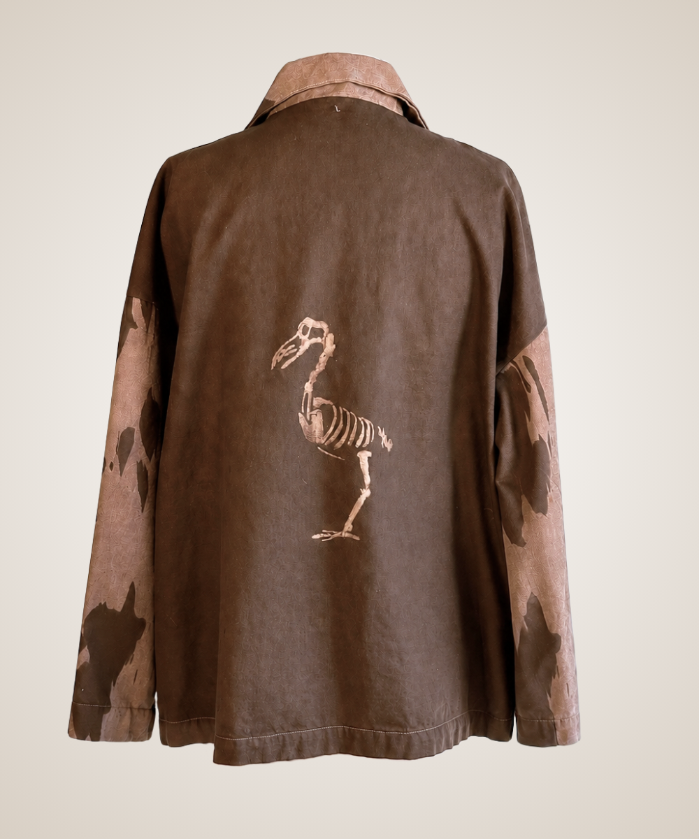 A brown jacket shown from the back, featuring a beige dodo bird skeleton graphic printed on the center back and a beige camouflage pattern on the sleeves, set against a plain light beige background.