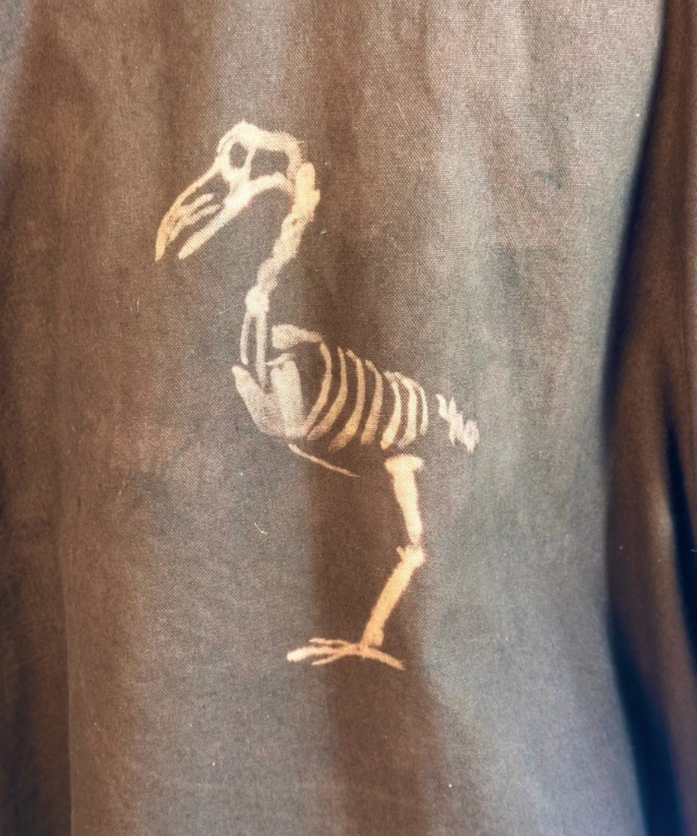 A close-up of a dark brown textured garment featuring a light tan bird skeleton graphic printed on the side.